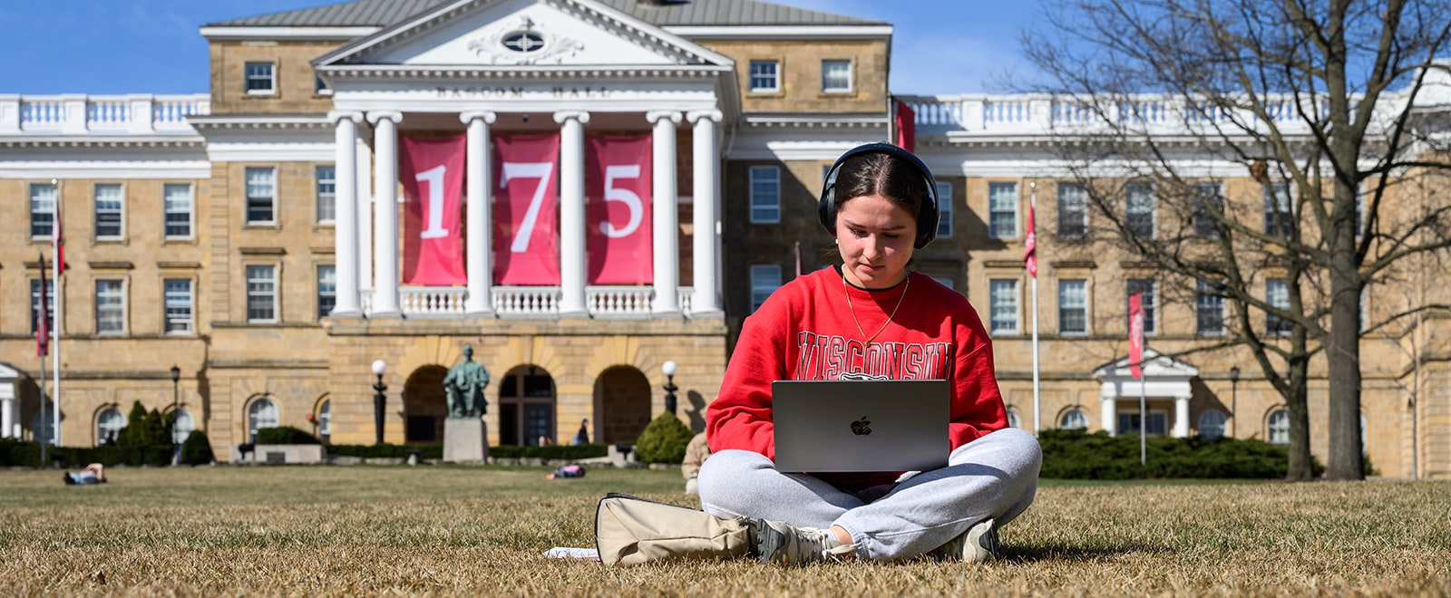 A student studies on Bascom Hill on an early spring day with Bascom Hall, adorned with 175 banners, behind her.