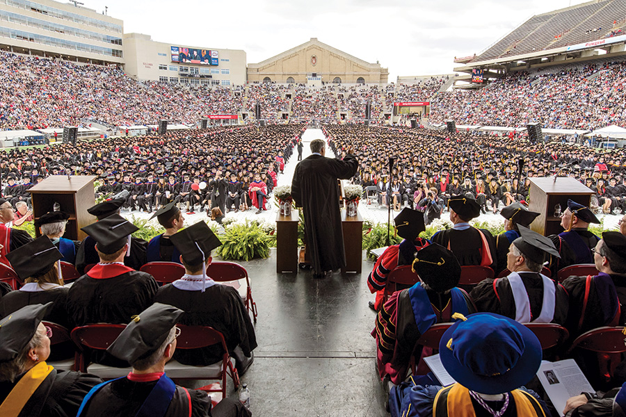 The view from the back of the stage at commencement at Camp Randall; the commencement speaker gesturing to hundreds of seated graduates in front of him.