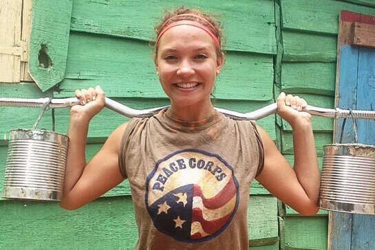 A person wearing a Peace Corps T-shirt holds a makeshift barbell over their shoulders.