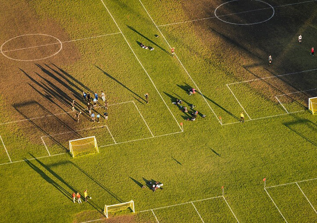 An aerial photo looks down on the Near West Fields as students are gathered on a soccer field. Their bodies cast long shadows in the late afternoon sun.