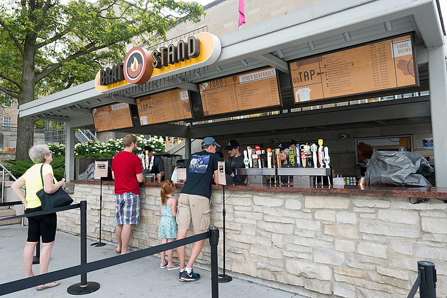 People standing in line ordering food and beverages at the Brat Stand. 