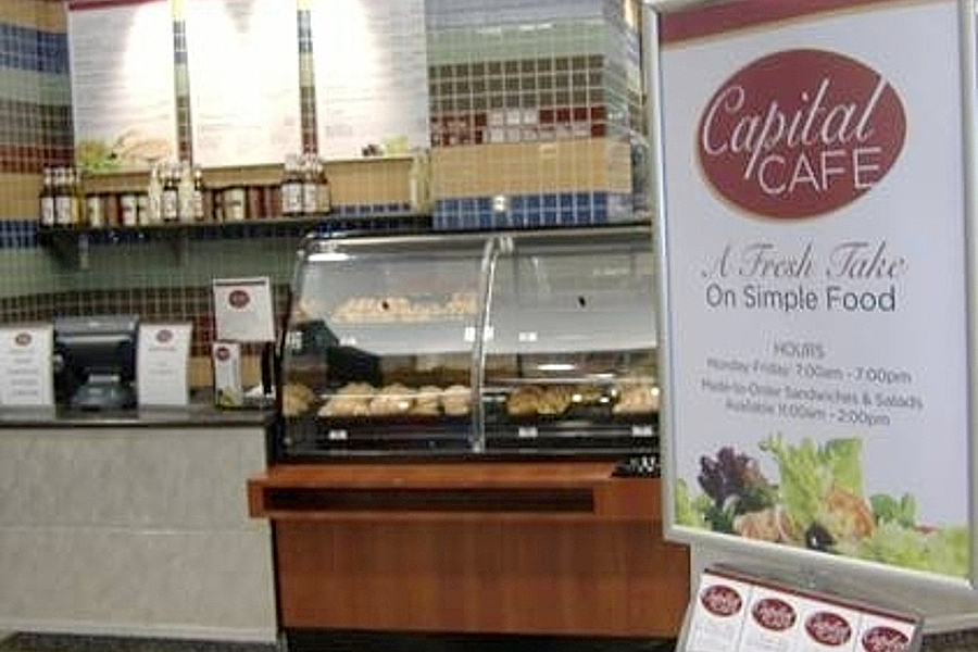 Food on display within glass case next to Capital Cafe sign containing restaurant hours.