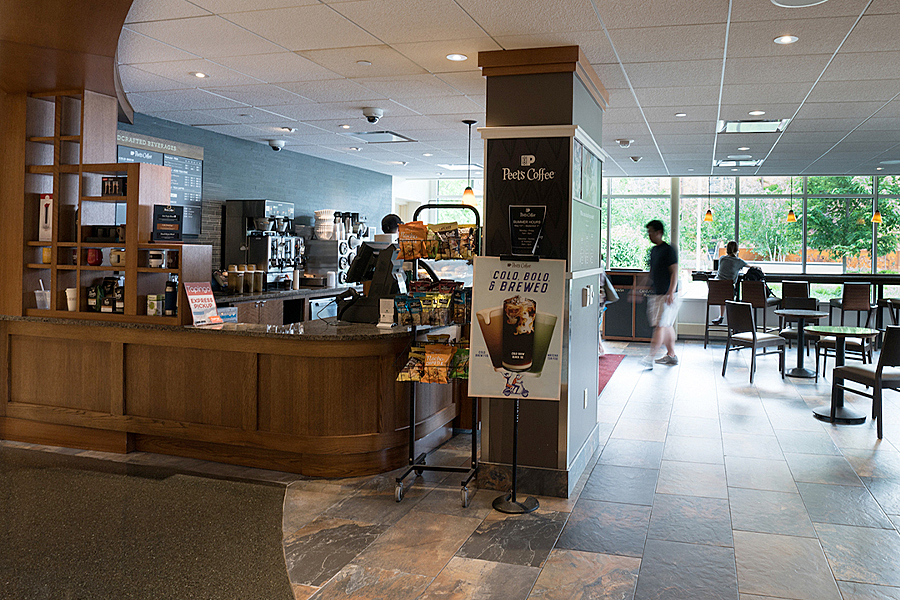 Sales counter at coffee shop with seating and large windows. 