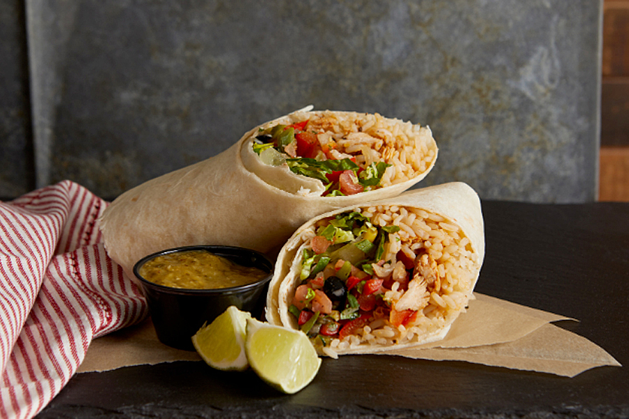 Two stacked burrito wraps next to limes and salsa. 