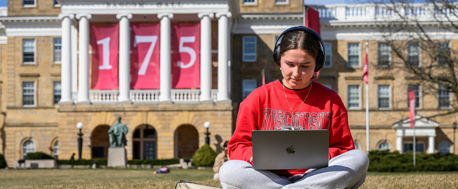 A student studies on Bascom Hill on an early spring day with Bascom Hall, adorned with 175 banners, behind her.