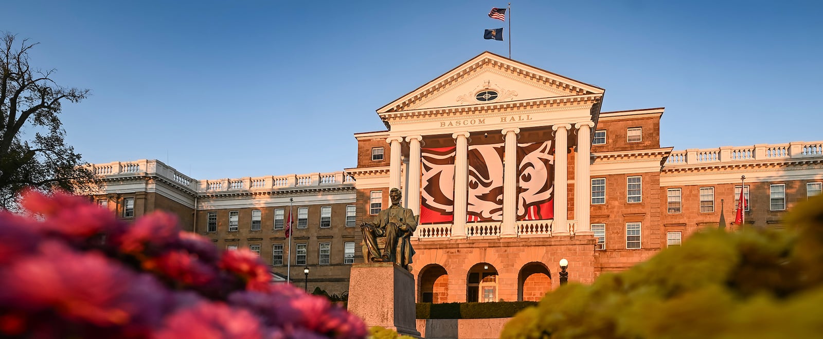 Bascom Hall, framed by red and yellow mums in the foreground, is touched by the first pink rays of sunrise on an autumn morning.