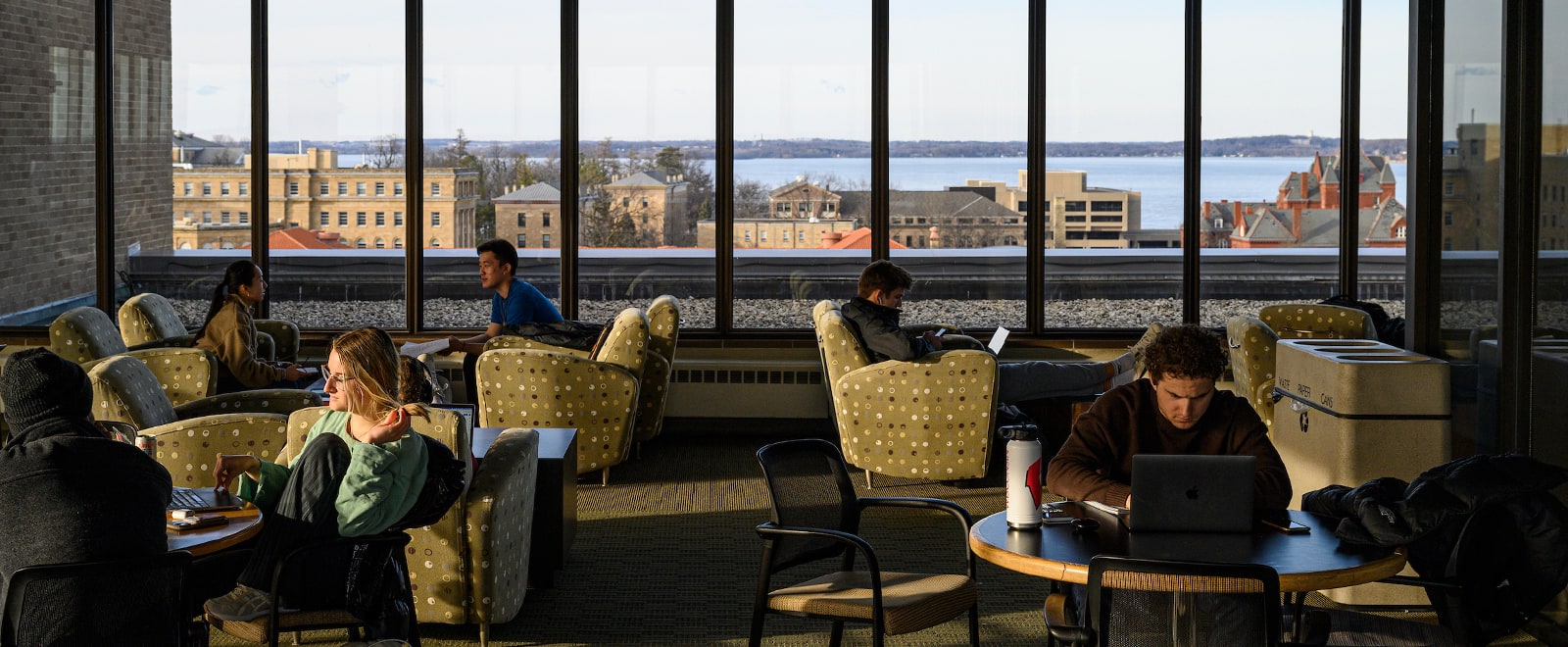 Students study in a lounge on the 13th floor of the Educational Sciences building with views of Lake Mendota in the background.