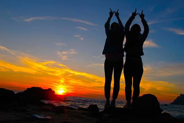 Two study abroad students making the W with their hands on a rocky beach