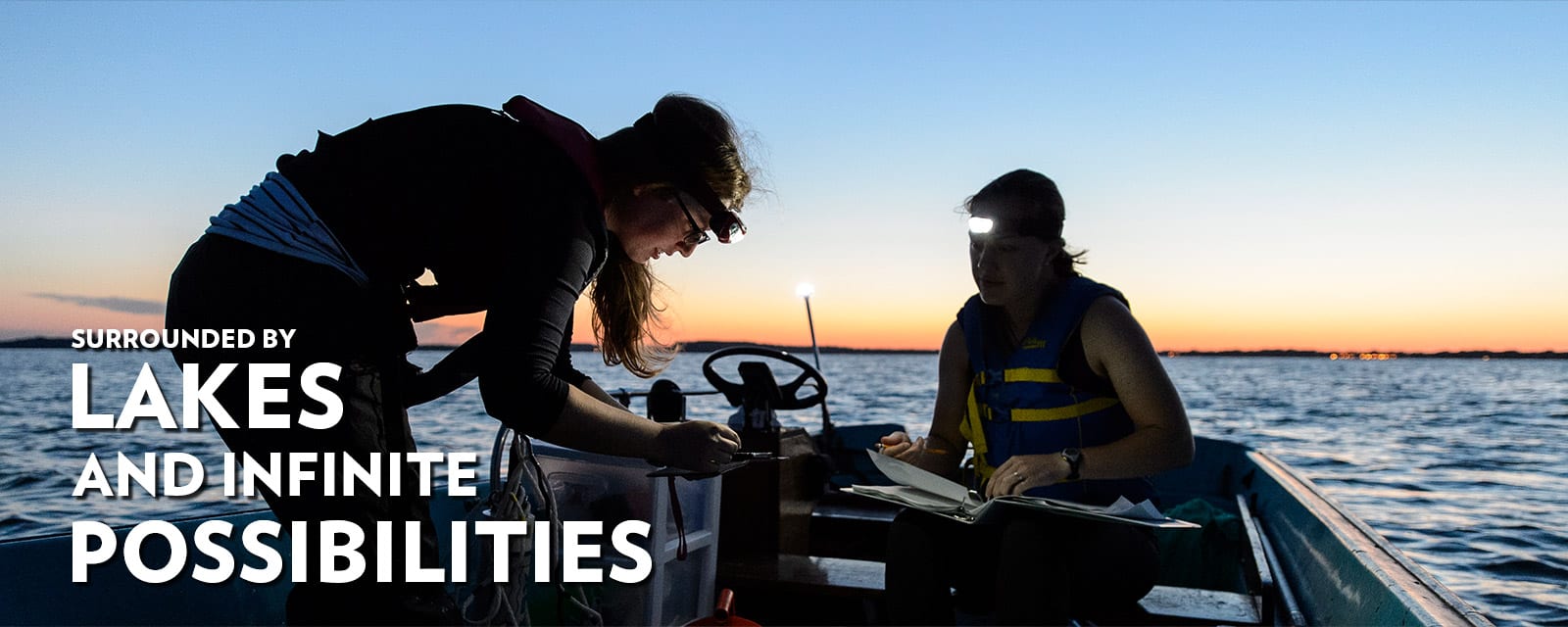 Two students doing research on a small boat at dawn with the words surrounded by lakes and infinite possibilities