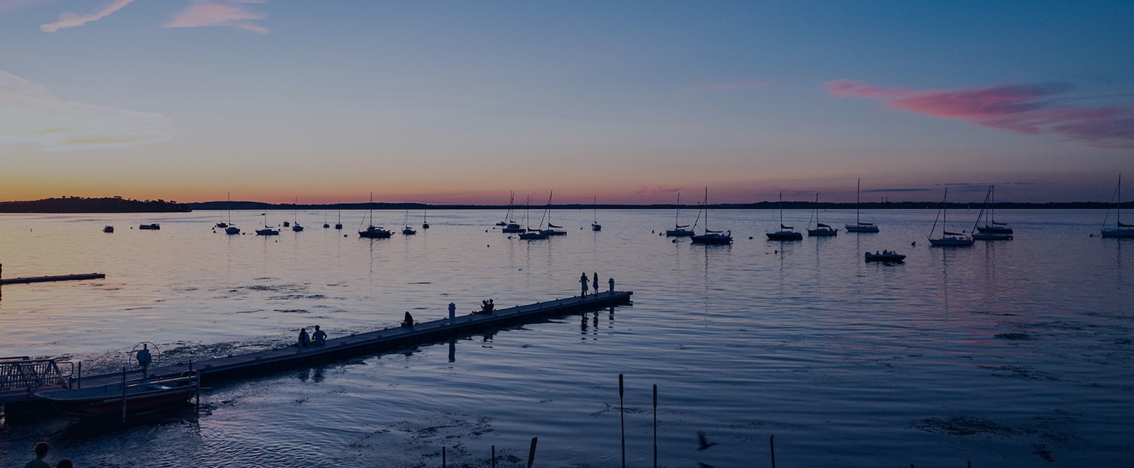 Sailboats rest at anchor on Lake Mendota under a summer evening sky as daylight fades into a palette of blues and pinks.