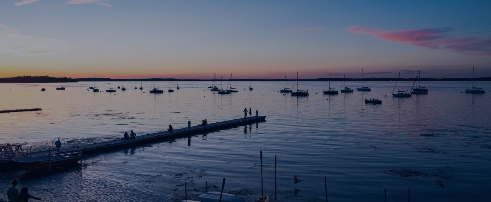 Sailboats rest at anchor on Lake Mendota under a summer evening sky as daylight fades into a palette of blues and pinks.