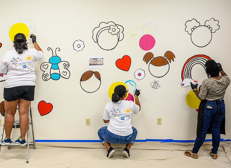 Three women begin to paint a colorful mural of hearts, flowers, butterflies and faces.