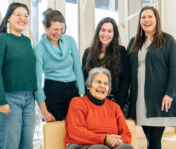 Ada Deer, seated, with interviewers standing behind her, laughing together.