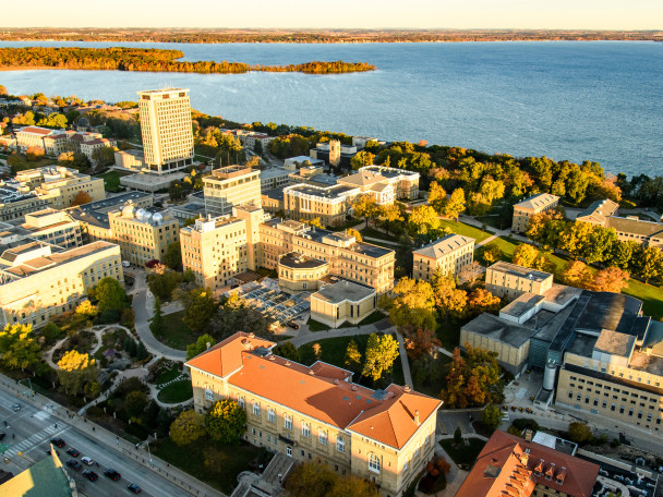 An aerial photo of the University of Wisconsin-Madison campus, including Lathrop Hall and Birge Hall, are pictured in early morning light. Lake Mendota lies in the background.