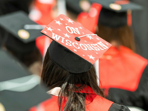 Student with a red, decorated graduation cap sits amongst a crowd during Commencement.