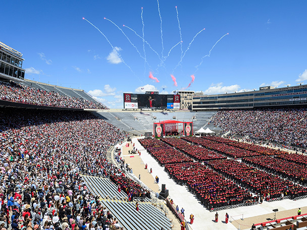 Fireworks burst in blue skies above a stadium filled with graduates and their guests.