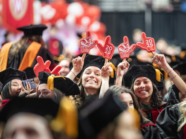 A photo of some smiling, gleeful people in graduation gowns holding up foam fingers.