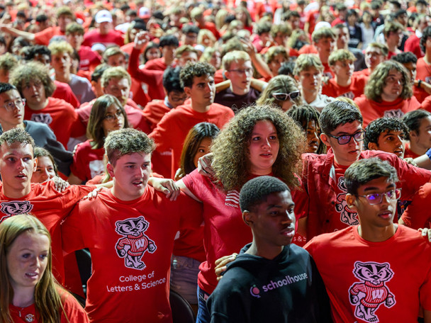 Rows of students wearing red Wisconsin Badgers shirts link arms while singing 'Varsity.'