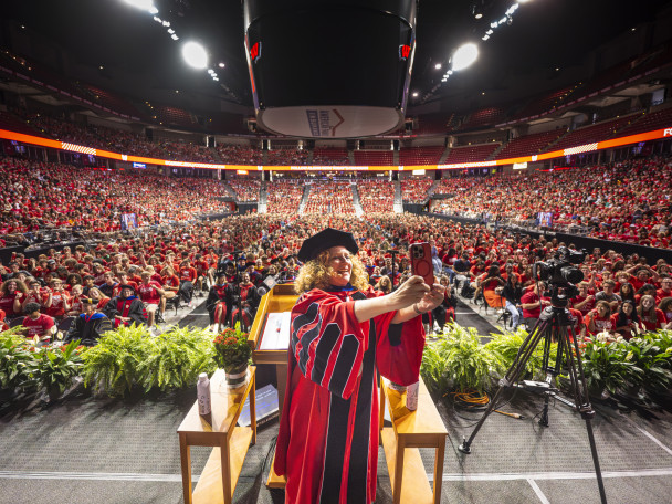Chancellor Mnookin holds up her phone and takes a selfie of herself and the thousands of students standing in the Kohl Center behind her.