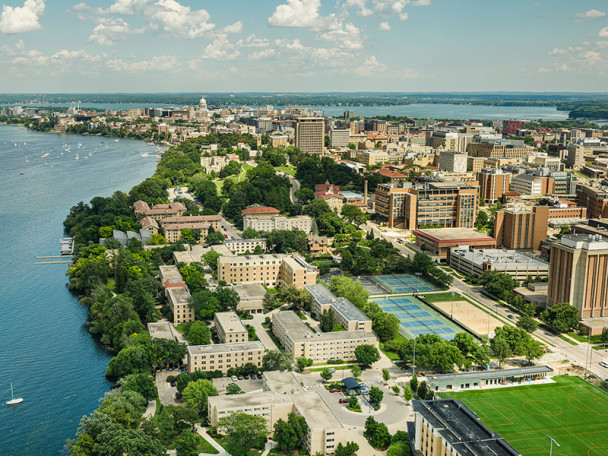 An aerial photograph taken by drone shows Cole Beach, Lakeshore Tennis Courts and the Lakeshore neighborhood with the Capitol and the campus skyline in the horizon on a partly cloudy summer day.