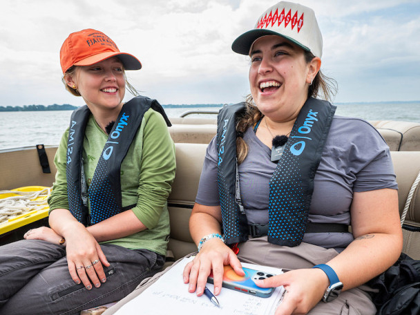 Two smiling people sitting on a boat. One holds work papers and a phone.