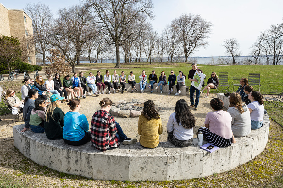 A First Nations Cultural Tour guide holds up a map of Wisconsin to a group sitting outdoors, in a circle.