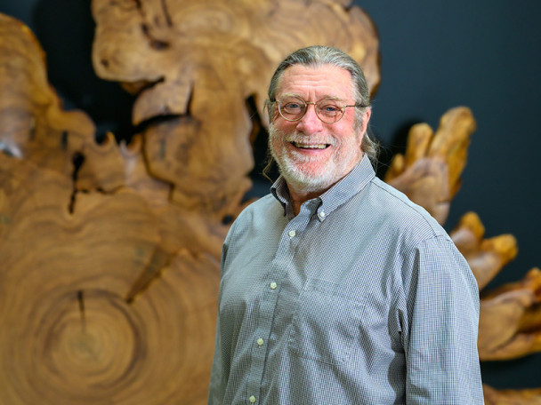 Brian Fox stands in front of a horizontal cross-section of a large, irregularly-shaped tree.