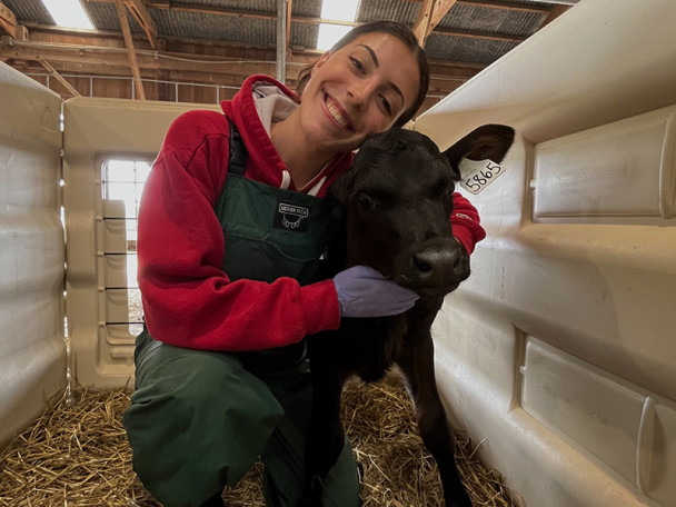 Lauren Jacobs hugs a black calf in a barn.
