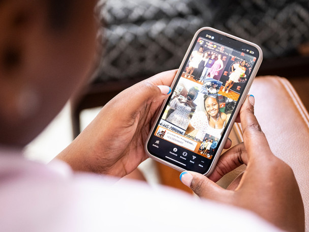 Tinnon sits on a chair holding her phone. Over her shoulder, the screen shows an in-focus look at her social media page.