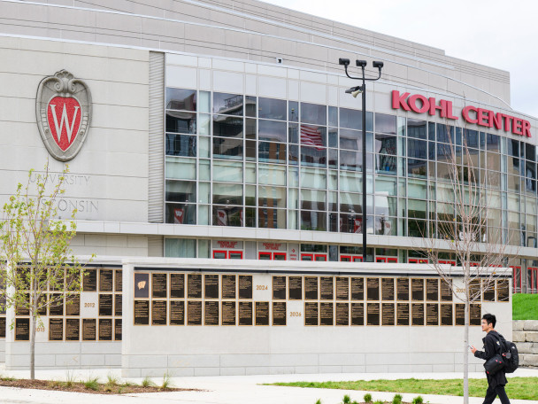 The UW Athletic Hall of Fame installation in front of the Kohl Center, with a person walking by.