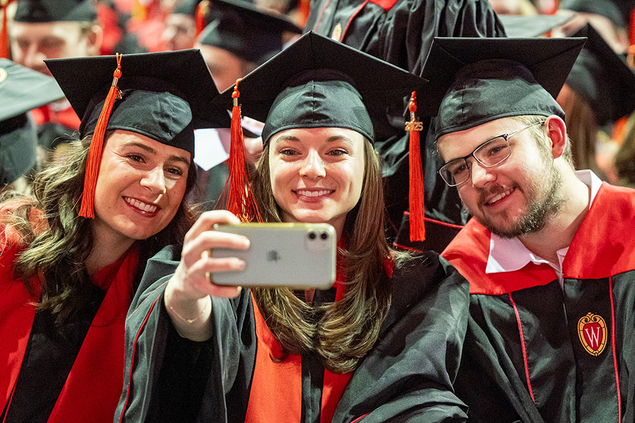 Three graduates in academic regalia lean together to take a selfie.