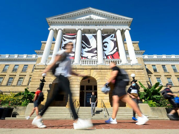 Several students walking quickly past Bascom Hall under a banner of Bucky Badger