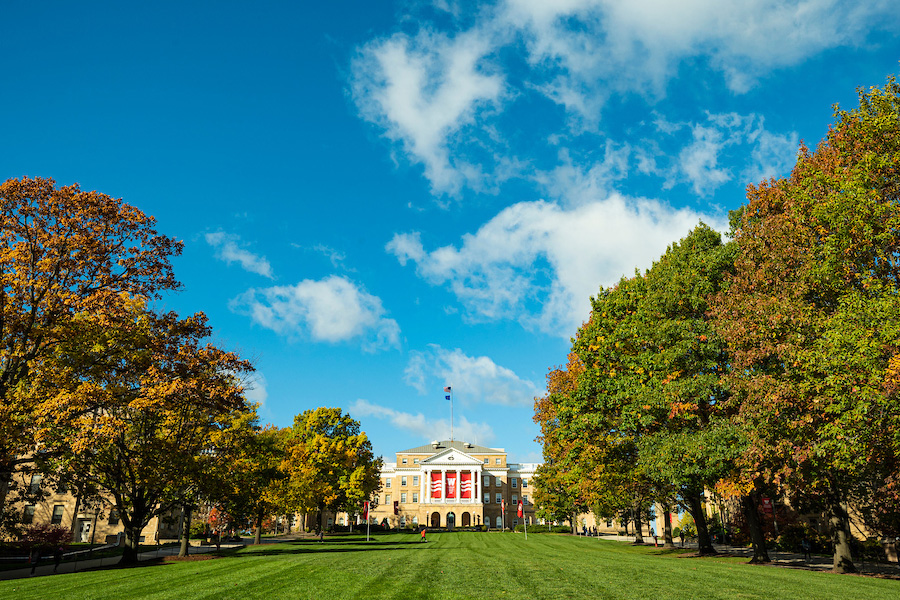 Long view of tree-lined Bascom Hill with Bascom Hall at the top against a blue summer sky