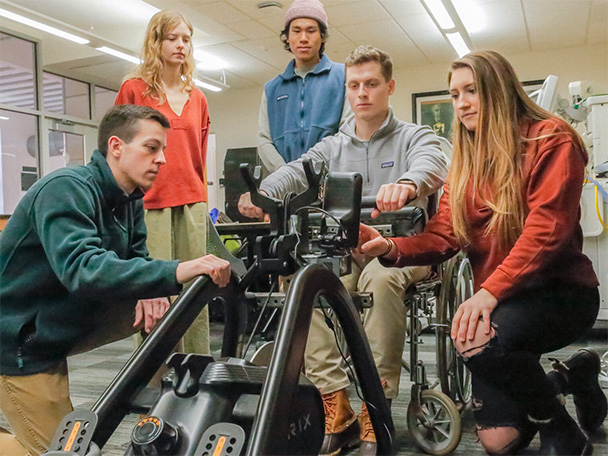 Biomedical engineering undergraduate students demonstrate a modified rowing machine that can be used by people in wheelchairs.