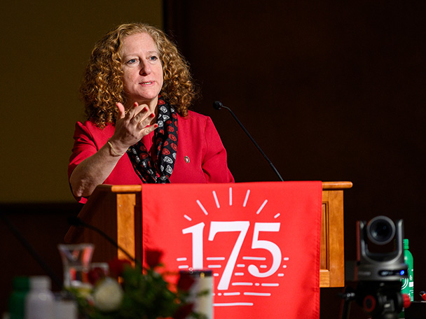 Chancellor Jennifer Mnookin gestures from behind a podium draped with a UW 175 banner.