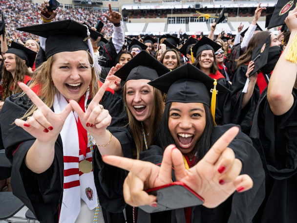 Graduates hold their hands in a W shape while smiling and laughing in Camp Randall Stadium.