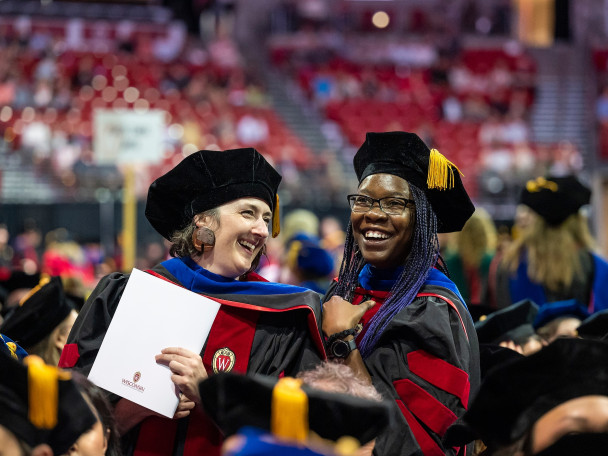 Two women in graduation robes smile happily.