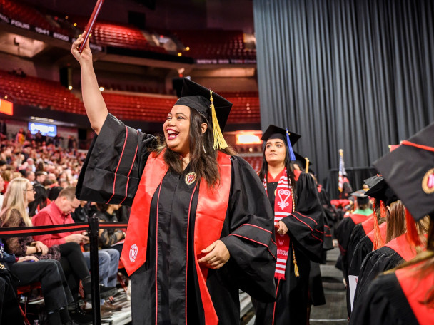 A woman holds up her diploma and shouts in glee.