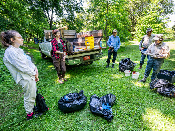 Four people stand in a semicircle outdoors listening to Wulfsberg read instructions from a paper in her hand.