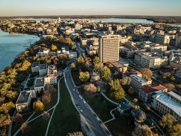 Aerial view of the UW Campus and beyond -- a cityscape with a mix of modern buildings, tree-lined streets, and lakes on either side.
