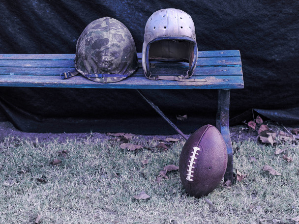 A World War Two helmet sits on a bend next to a vintage football helmet. On the ground lies a football.