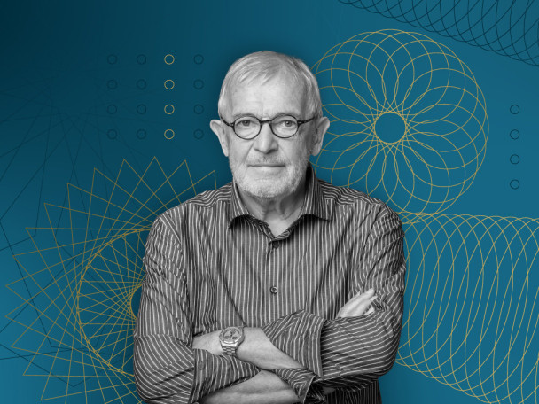 Portrait of UW–Madison physicist Francis Halzen wearing glasses and a striped button-down shirt with his arms crossed, set against a blue background with yellow geometric line art designs.