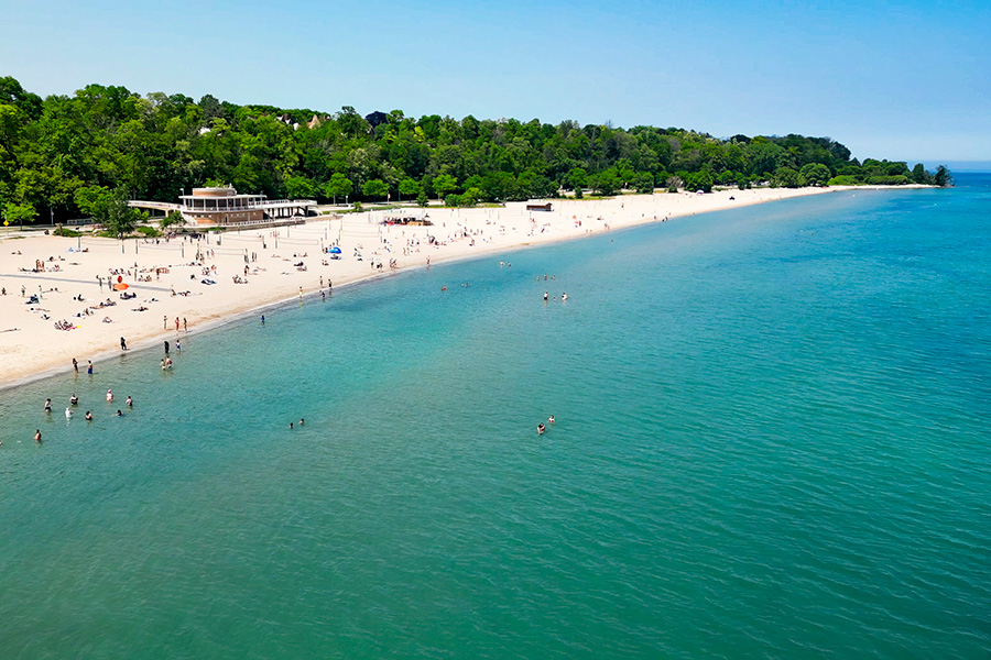An aerial view of a beach along Wisconsin's coast. People play in the water while others lay on the sandy beach.