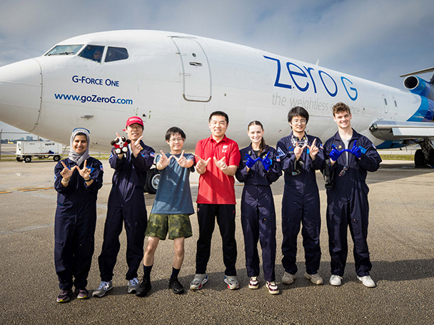 Seven engineering students pose on an airport runway tarmac beside G-Force One.