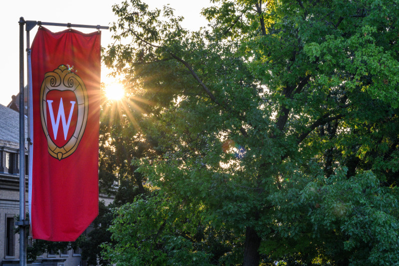 The sun emerges between a banner with the UW crest logo and a. tree line.