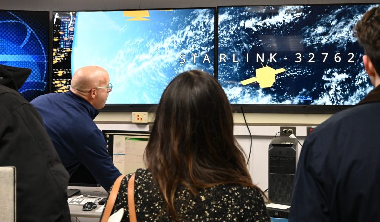 A group stands in front of large TV screens that display Starlink satellites.