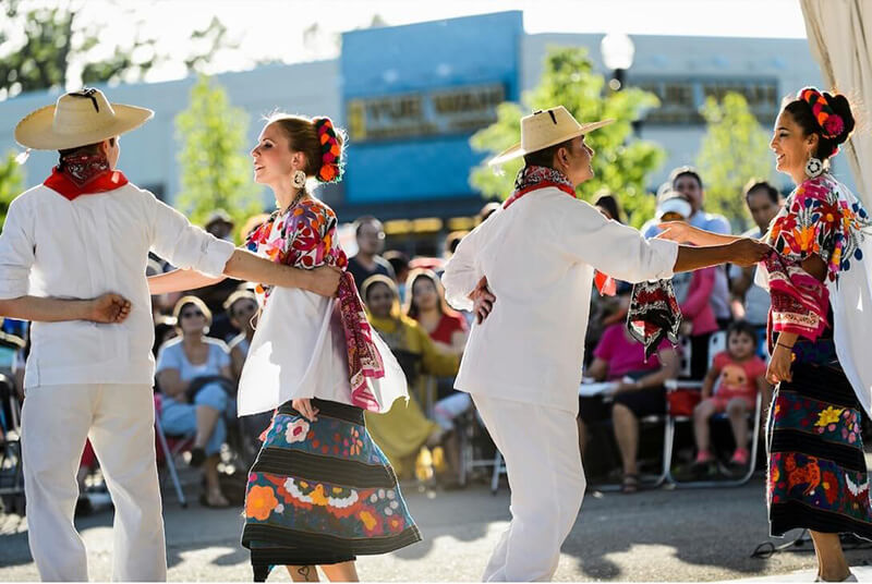 Four dancers in traditional Latin dress perform outdoors during a South Madison event